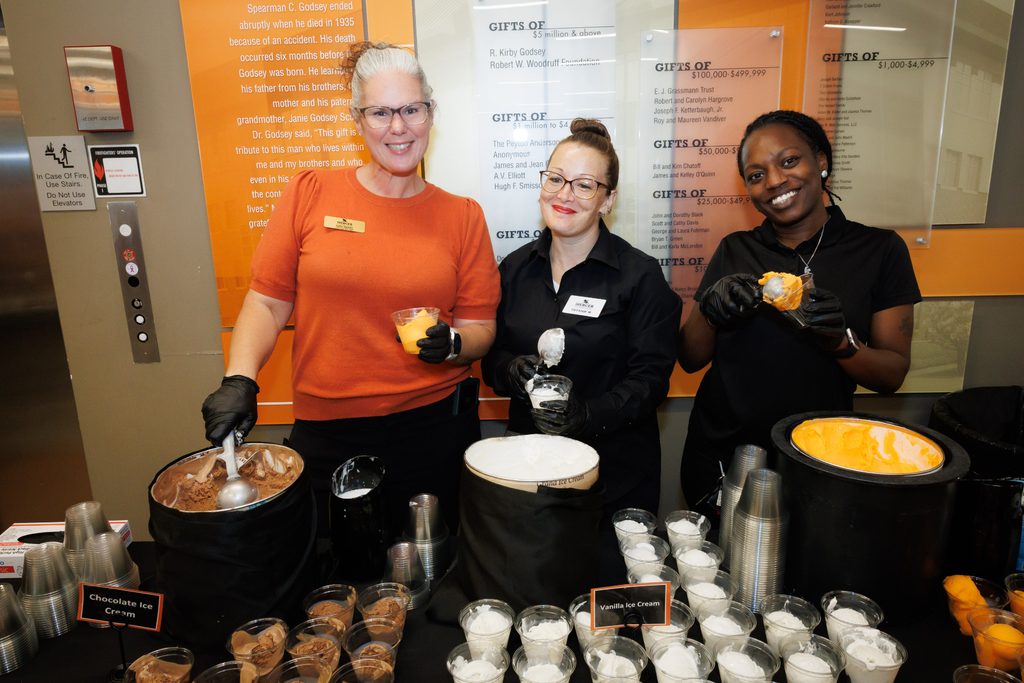 Three staff members serving scoops of chocolate and vanilla ice cream into clear cups.