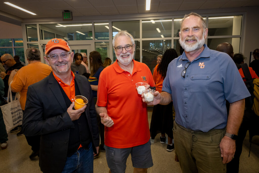 Three faculty members standing together in a lobby, each holding a small cup of ice cream.