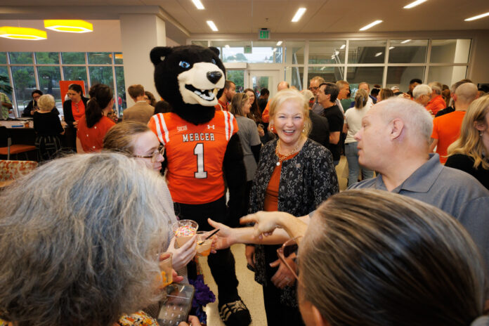 261009MUIceCreamSocial_0008 A Mercer University bear mascot stands in a crowded room with people, including the Mercer president, holding small ice cream cups.