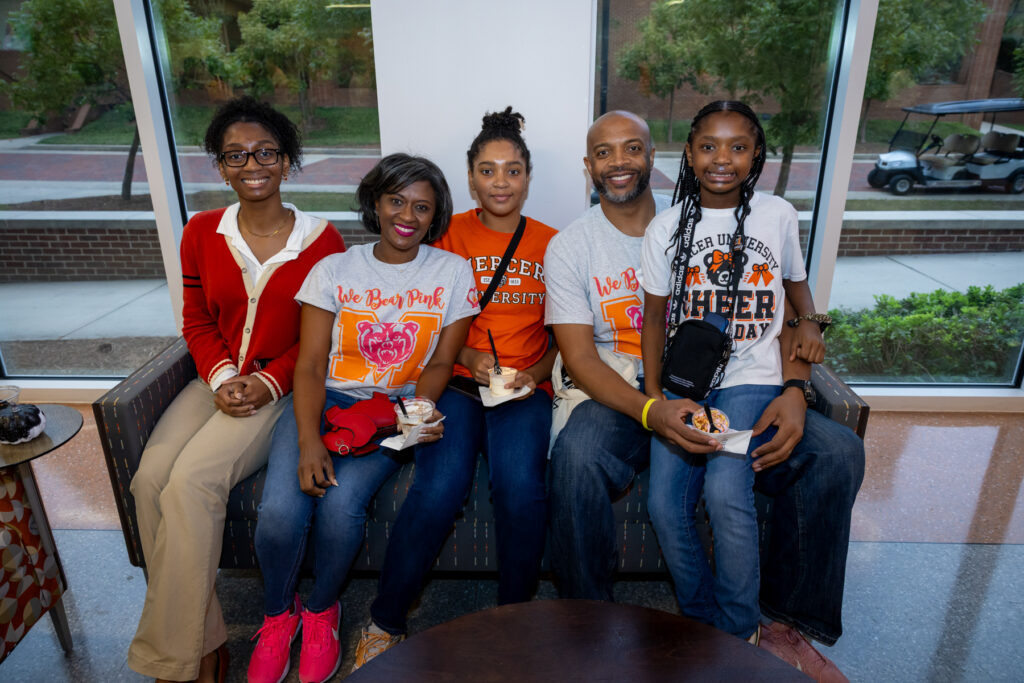 Five people sitting on a couch in Mercer University apparel.