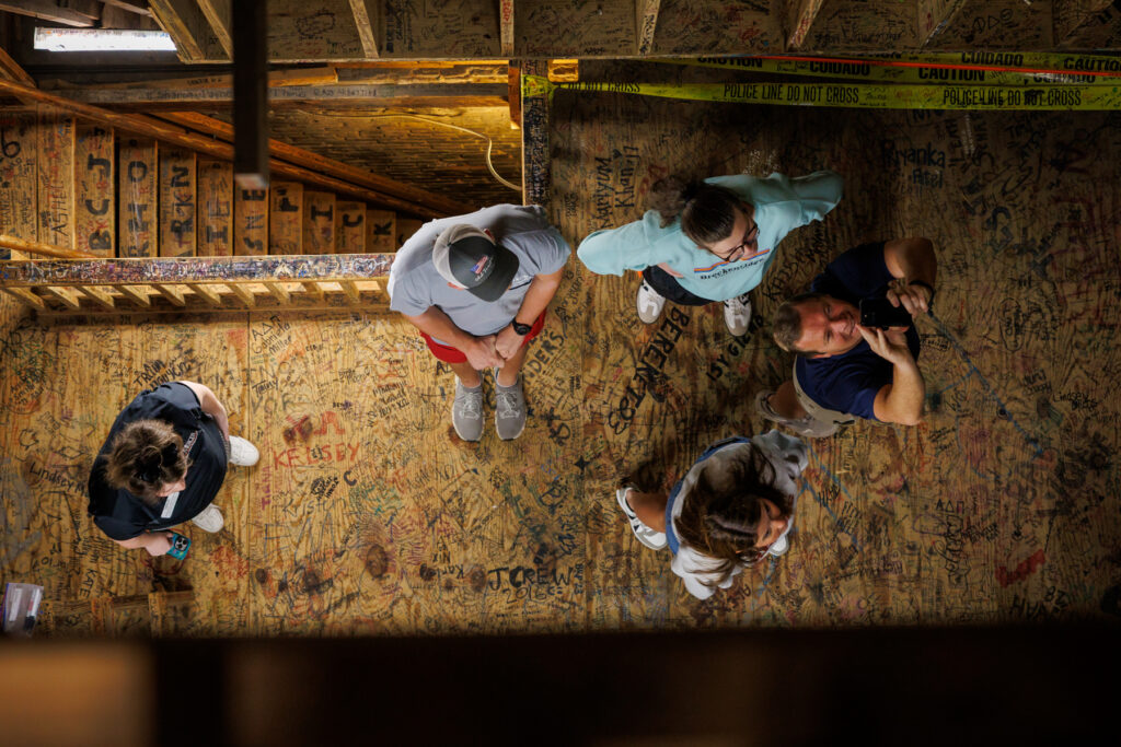 Four people stand on a wood floor covered in handwritten signatures and messages.