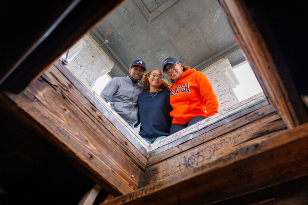 Three people looking down into a wooden structure covered in signatures.