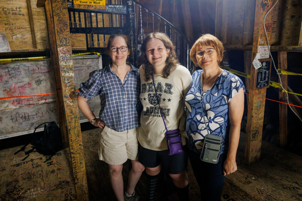 Three people standing together inside a wooden tower covered in signatures.