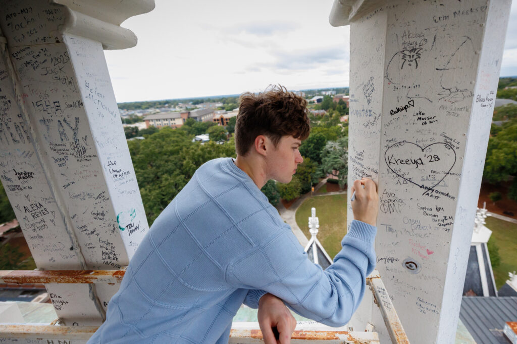 A student writes on a white pillar covered in signatures, overlooking Mercer's Macon campus.