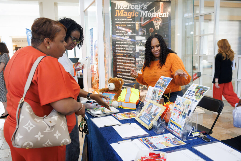Three women at a table displaying informational brochures and a teddy bear.