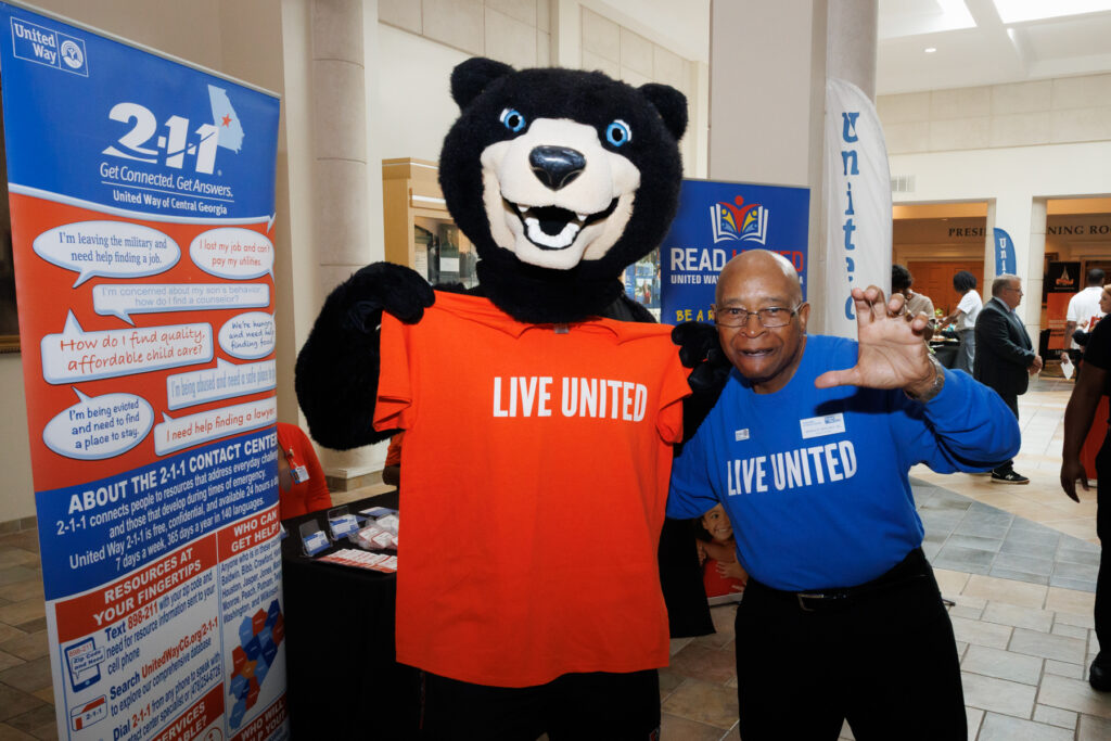 Toby and a man in a blue shirt holding an orange LIVE UNITED T-shirt.