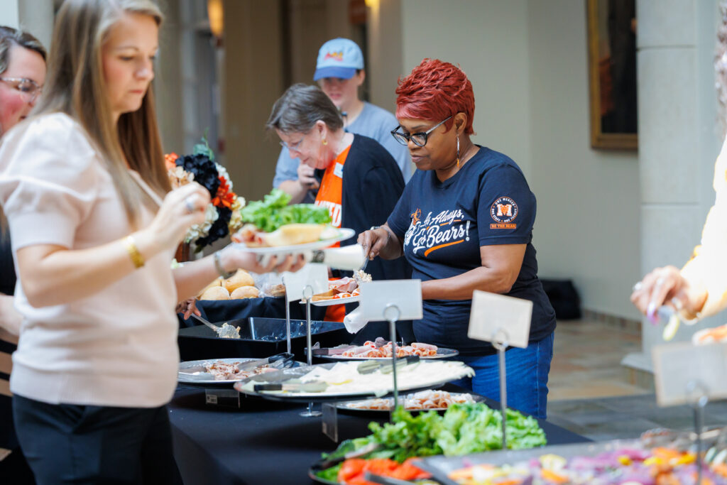 People serving themselves at a buffet with various platters of food.