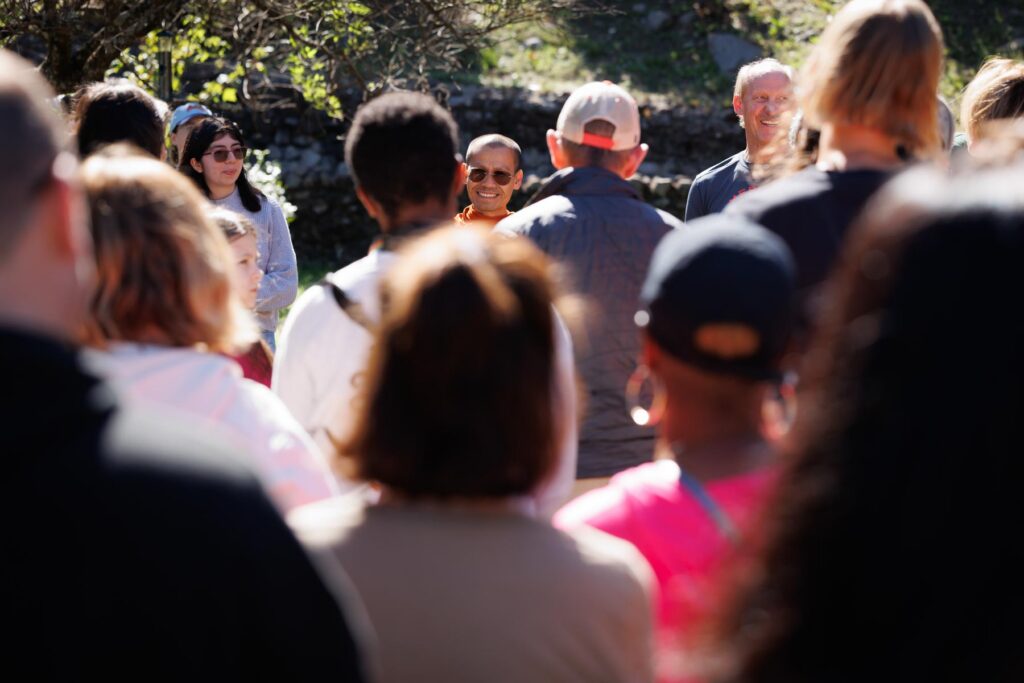 A group of people standing outdoors, looking toward a smiling person in orange robes.