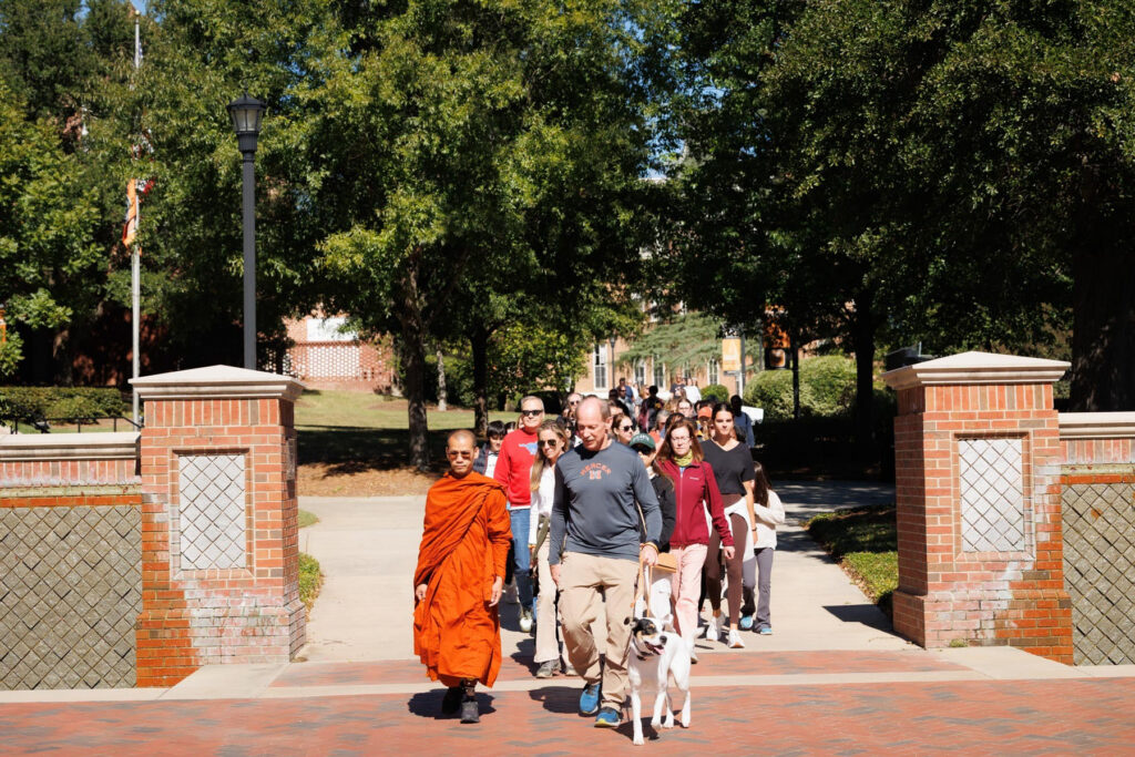 A Buddhist monk and a group of people walking together on a campus path.