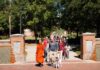 Monk teaches meditation, leads Community Peace Walk during Mercer visit A group of people walking through a brick campus gate, including a monk in orange robes and a man walking a dog.