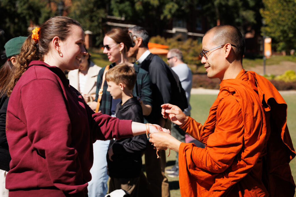 A Buddhist monk tying a string bracelet onto a Mercer student's wrist.