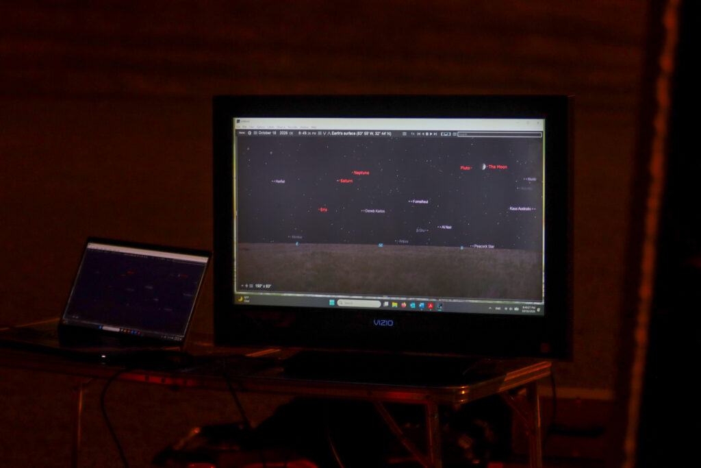 A laptop and a monitor displaying star charts of the night sky on a folding table.