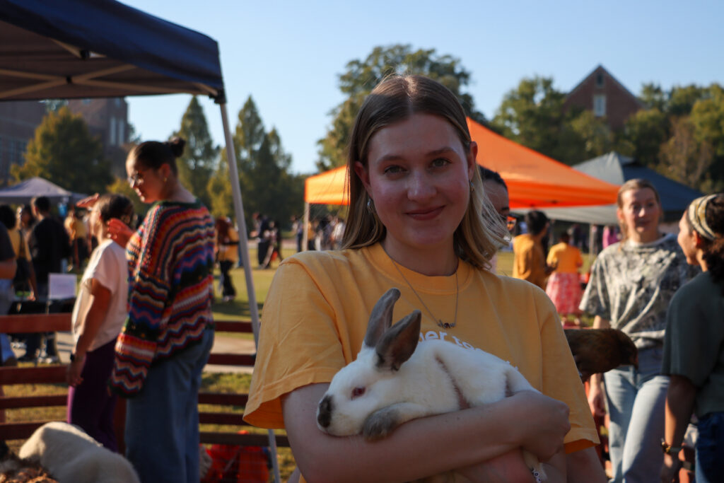 A Mercer student holds a white rabbit at an outdoor event.