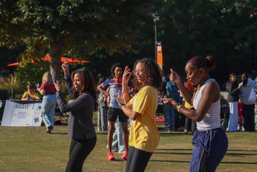 Three young women dancing outdoors on a grassy lawn.