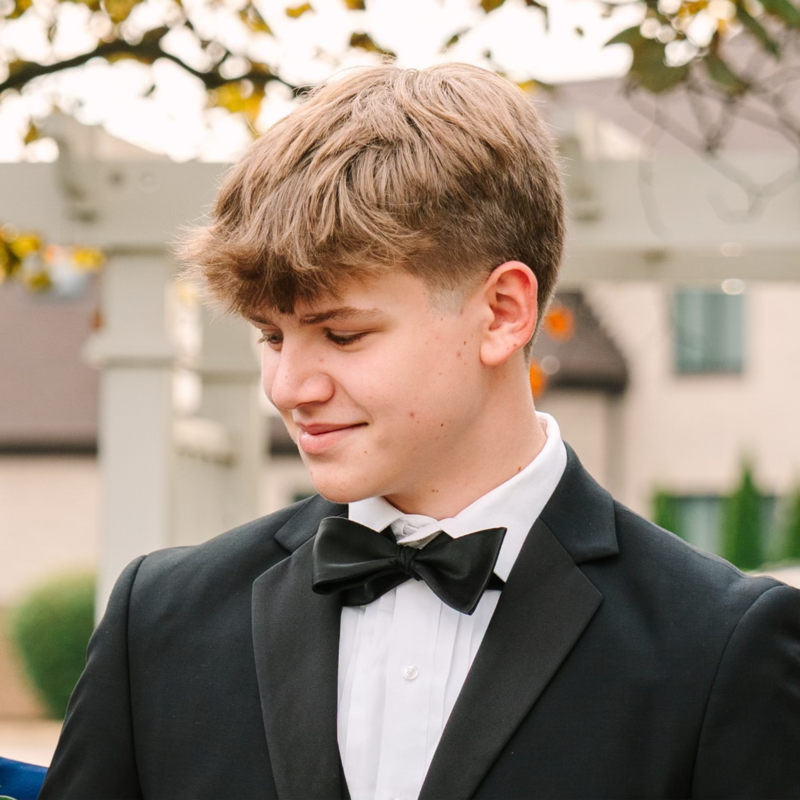 A young man in a tuxedo with a black bow tie looking down.