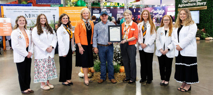 Group of seven people posing for a photo, with one person holding a framed certificate at an agricultural trade show.
