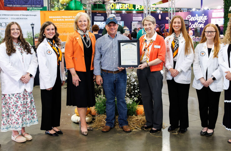Group of seven people posing for a photo, with one person holding a framed certificate at an agricultural trade show.