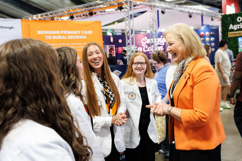 President Penny L. Elkins, Ph.D., laughs while talking to a group of medical students wearing white coats.