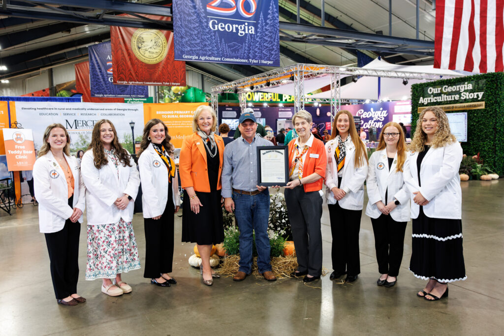 A group of people, including some in white medical coats, pose with a framed document at the Georgia National Fair.
