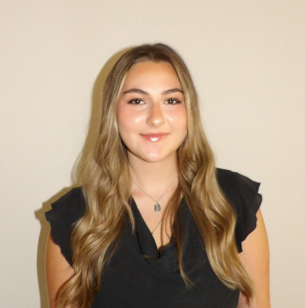 A young woman with long wavy hair wearing a black top and a silver necklace.