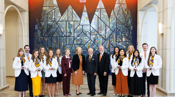 School of Medicine celebrates 2026 Nathan Deal Scholars A group of students and faculty members in professional attire posing for a photo in front of a stained glass mural.