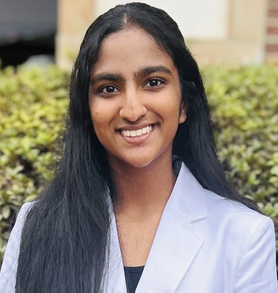 A young woman with long dark hair smiling while wearing a white coat.