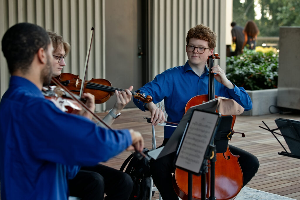 Strings musicians playing music together on a wooden outdoor terrace.