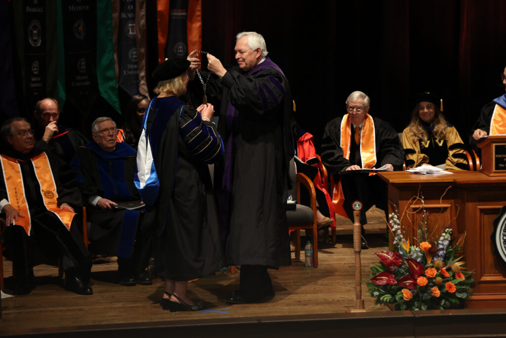 Mercer Chancellor William D. Underwood, in academic regalia, places the presidential medallion around President Penny L. Elkins' neck on a stage.