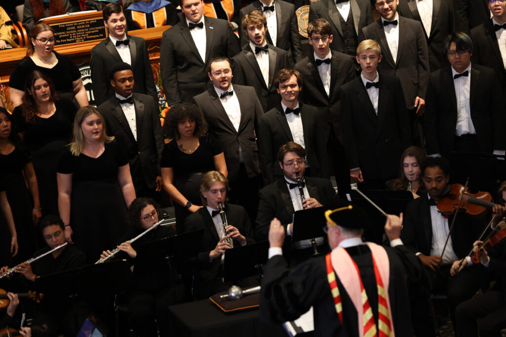 A formal concert choir and orchestra performing, led by a conductor seen from behind.