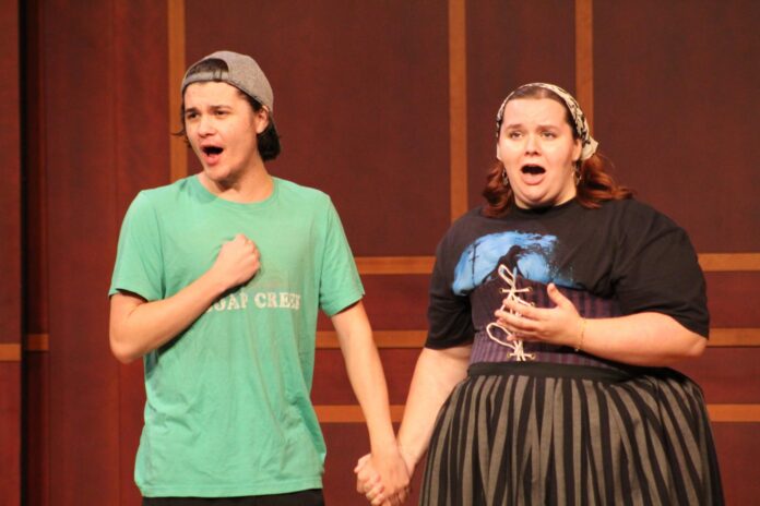 A young man and woman holding hands while singing on a stage.