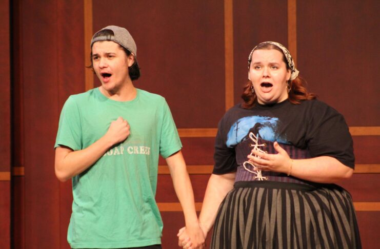 A young man and woman holding hands while singing on a stage.