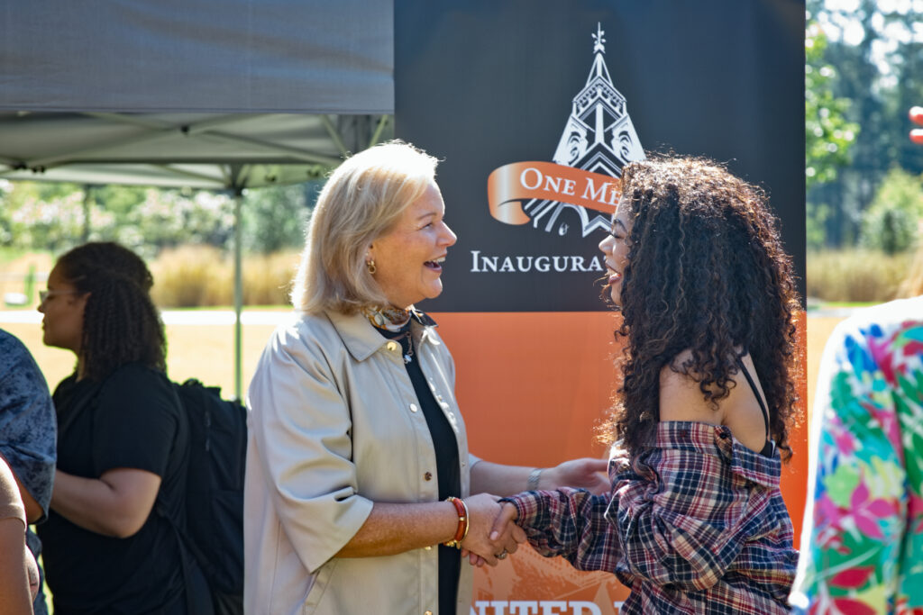 President Elkins and a woman shaking hands in front of an One Mercer inauguration banner.