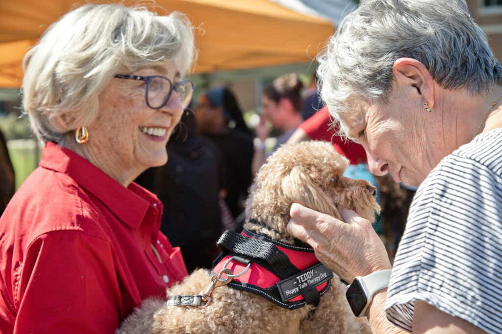 Two women petting a curly-haired therapy dog.