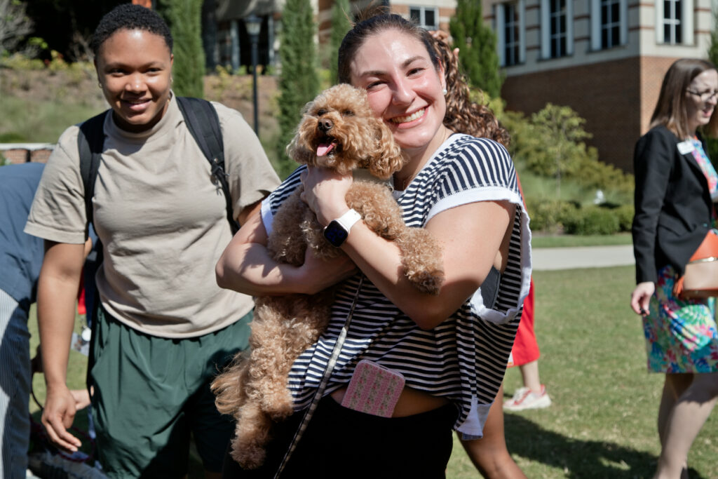 A woman smiling while holding a small, curly-haired dog.