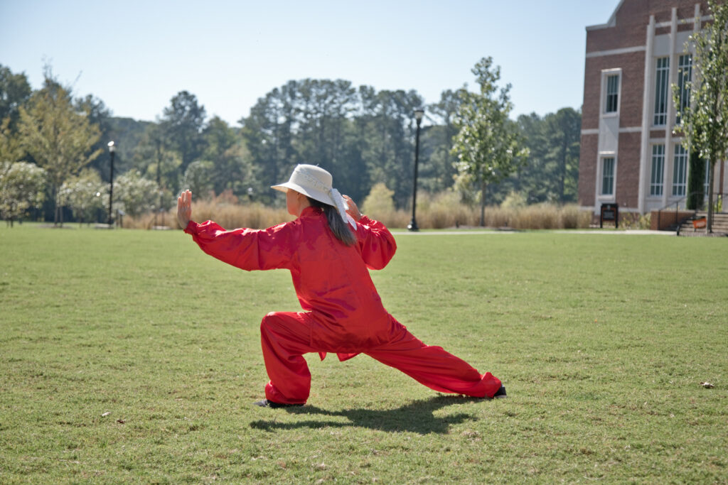 A person in a red uniform and a white sun hat practicing tai chi on the Upper Quad.